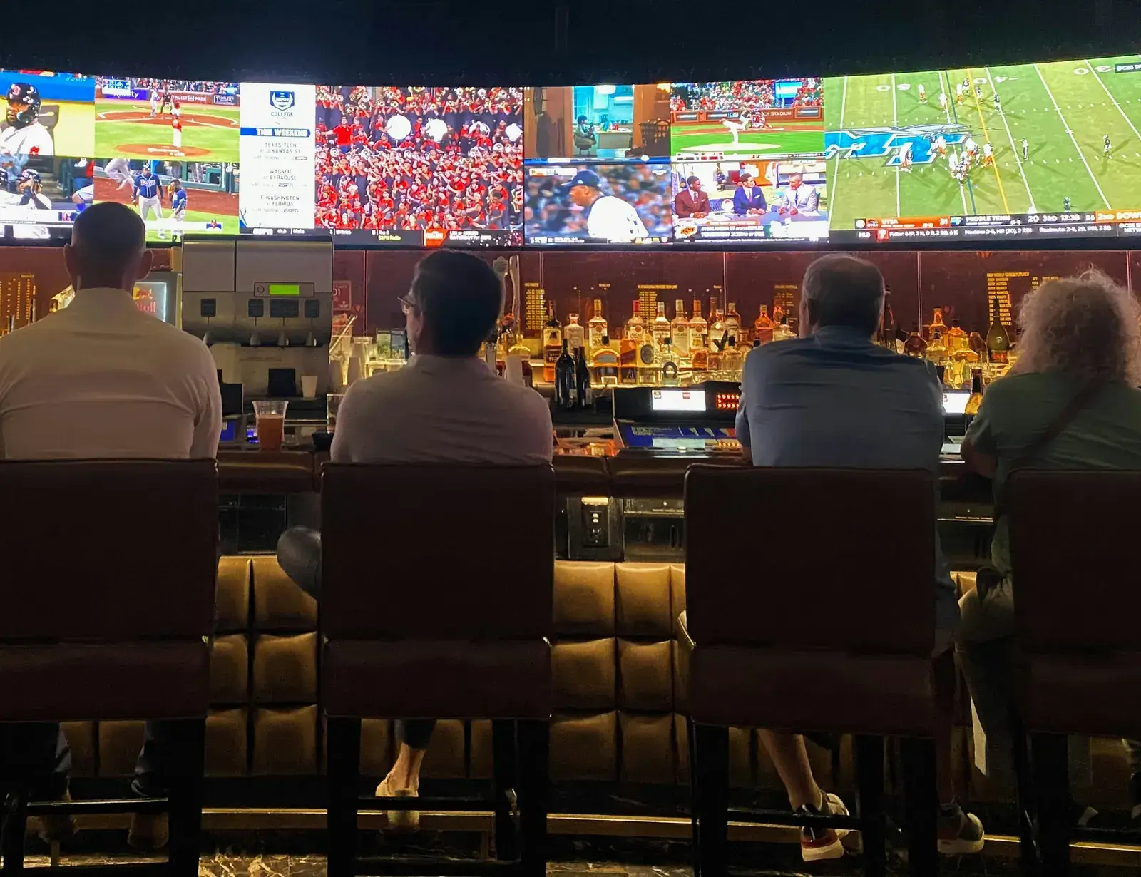 A group of people sitting at a bar watching several sporting events on TV